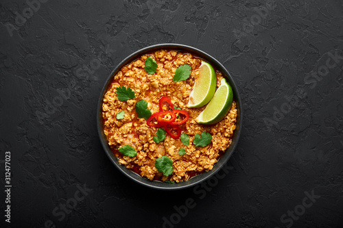 Chicken keema in traditional indian copper kadai at dark slate background. Kheema is indian and pakistani cuisine curry dish with minced meat and spices. Copy space. Top view