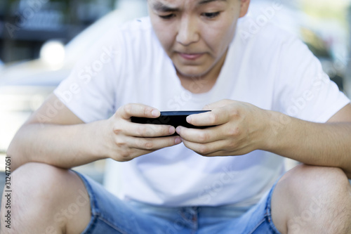 A man is sitting on the street playing a game on his mobile phone