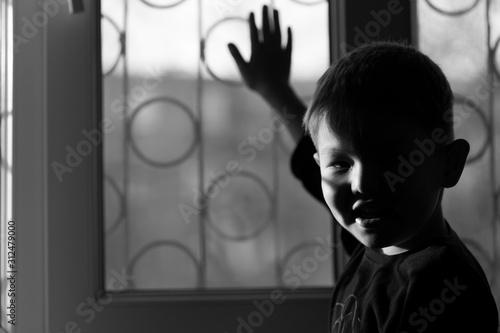 A boy stands and looks out the window at sunset