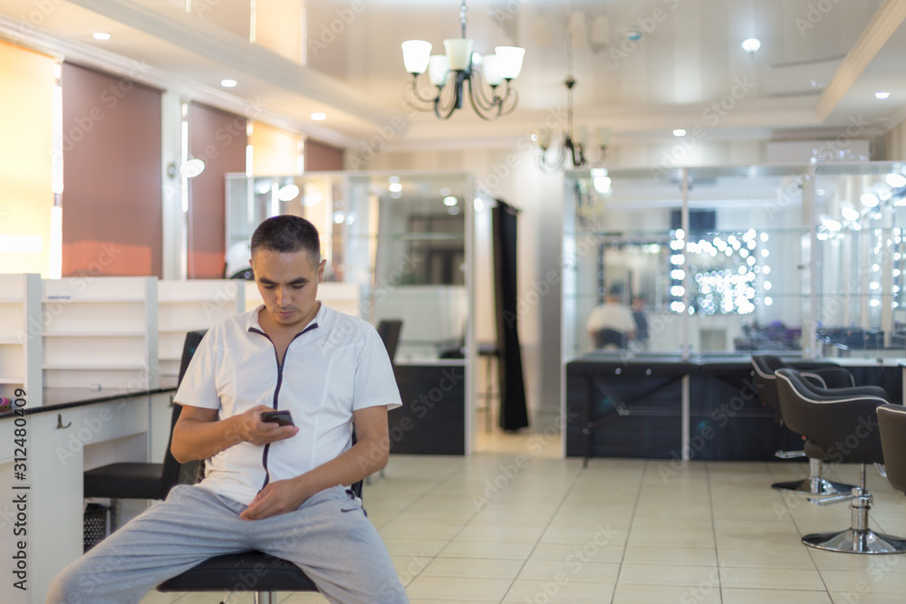 A man sits on a chair in the center of a beauty salon in the hands of a smartphone
