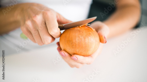 Young woman's hands peel fresh onion head on white background 