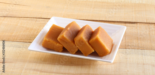 Mysore pak, a traditional, popular, and delicious sweet dish native to the city of Mysore, Karnataka, India, is made from ingredients like gram flour, ghee and sugar, on a ceramic plate.