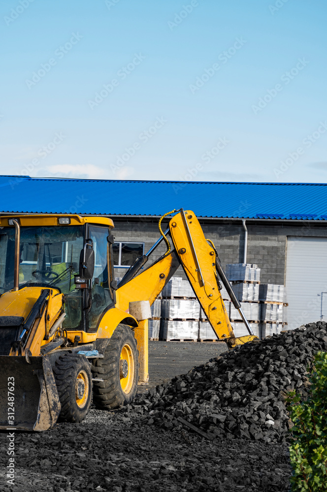 The yellow all-wheel drive backhoe loader stands on the yard ready for workind on construction site.