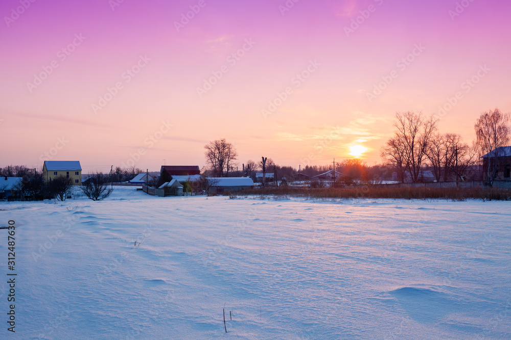 Rural landscape in the winter. The field is covered with snow. Village behind a field at sunset Rural landscape in the winter. The field is covered with snow. Village behind a field at sunset