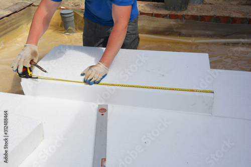 House floor layers construction with waterproofing membrane, styrofoam insulation boards. Worker measuring foam insulation board with measure tape