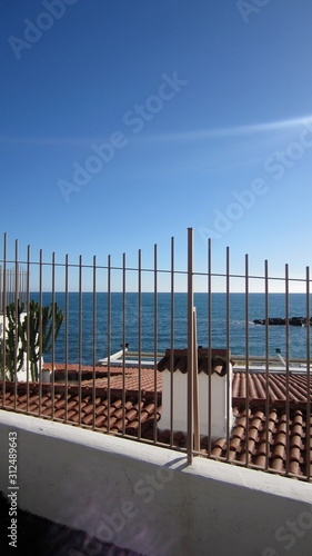 Metal fence of the house by the sea with a view of the roof, cactus and the sea on a sunny cloudless day