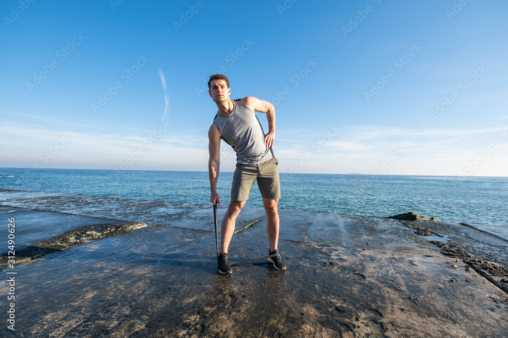 Young fit male training with  athletic rubber on the beach in summer day