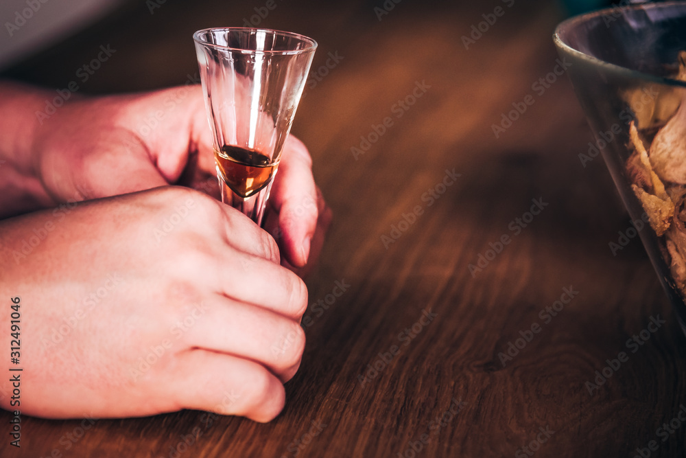 Obraz premium Drinking addiction - male hands playing with glass of his favourite alcoholic beverage - rum, whiskey or other liquor spirit and eating salted potato chips - modern unhealthy diet and lifestyle issue