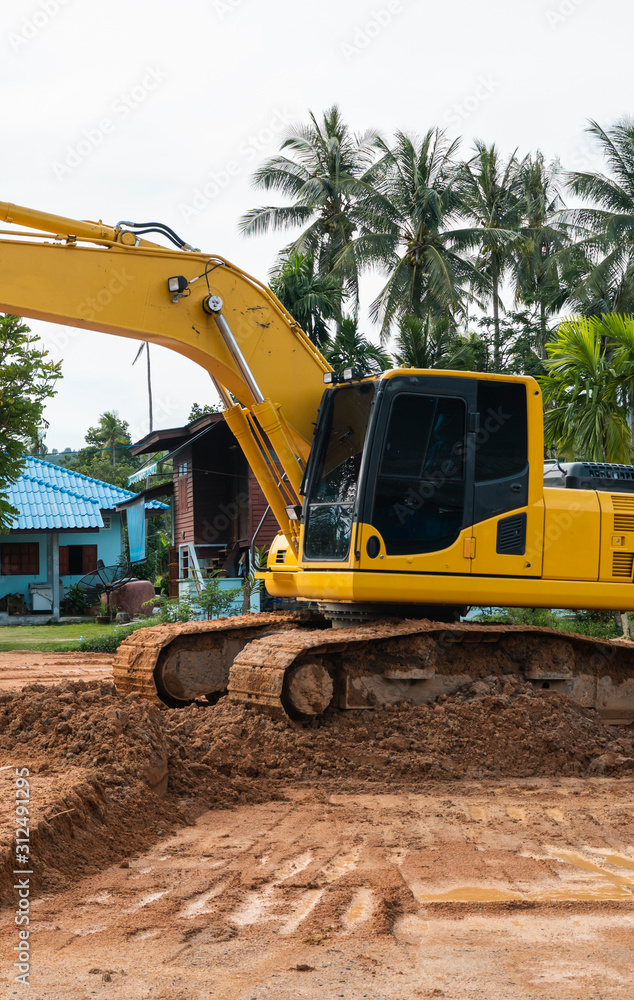 Obraz premium Yellow excavator on a construction site against blue sky. Heavy industry. Close up details of industrial excavator. Large tracked excavator standing on a orange ground with a palms on background.