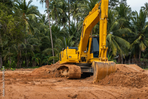 Yellow excavator on a construction site against blue sky. Heavy industry. Close up details of industrial excavator. Large tracked excavator standing on a orange ground with a palms on background.