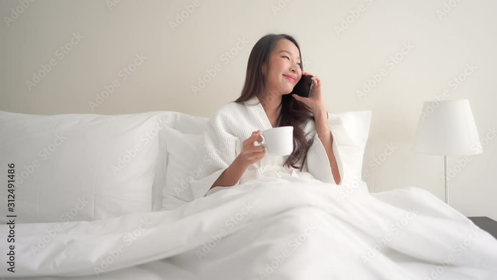 Asian lady having comfy cozy time on a hotel bed answering a phone call Asian lady having comfy cozy time on a hotel bed answering a phone call