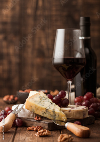 Canvas Print Glass and bottle of red wine with selection of various cheese on the board and grapes on wooden background