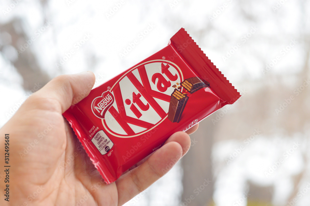 Kit Kat chocolate bar in male hand on snowy background. Kit kat created