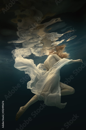 Girl in a beautiful dress swims underwater