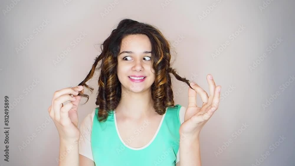 Attractive girl smiles for the camera wile playing with her hair. Beauty woman with wavy dark hair. Young girl with Healthy Thick Hair. Hairstyle, cure, extensions. slow motion Attractive girl smiles for the camera wile playing with her hair. Beauty woman with wavy dark hair. Young girl with Healthy Thick Hair. Hairstyle, cure, extensions. slow motion
