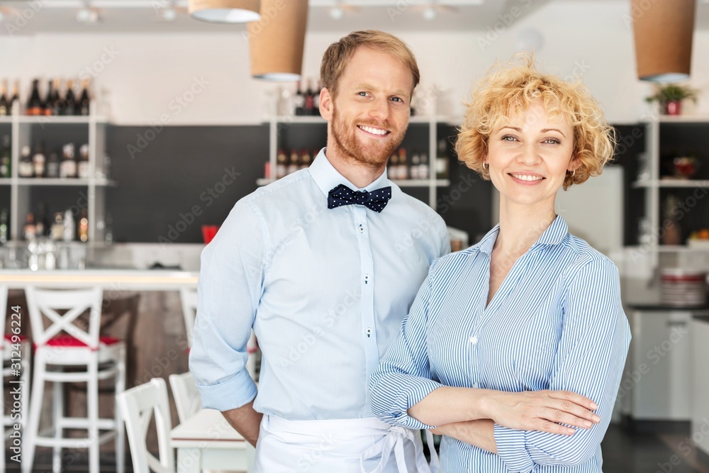 Obraz premium Portrait of smiling owner and waiter standing against furniture at restaurant