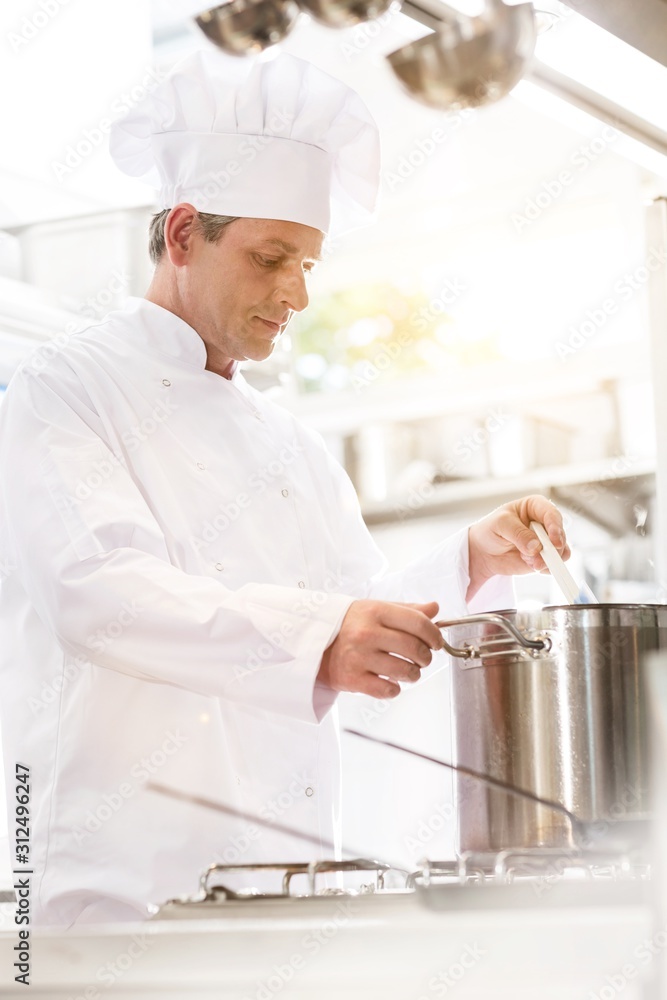 Confident mature chef cooking in steel pot on stove in kitchen at restaurant