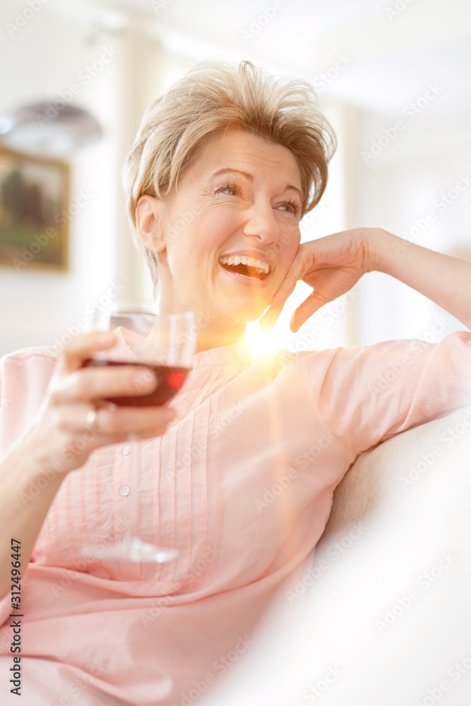 Cheerful mature woman holding wineglass while looking away at home Cheerful mature woman holding wineglass while looking away at home