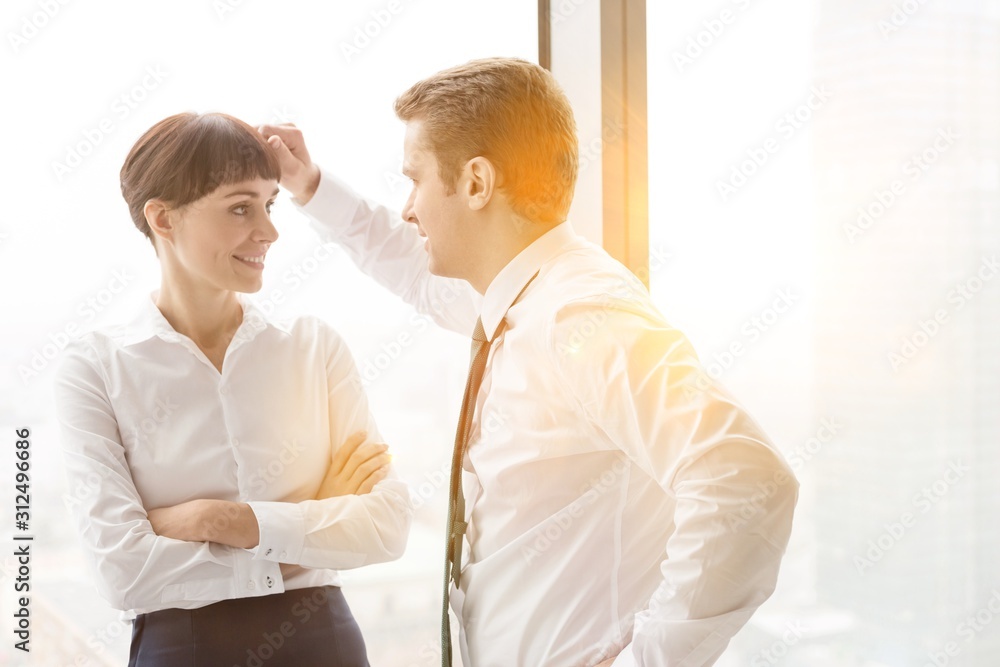Businessman flirting with businesswoman standing against window at modern office Businessman flirting with businesswoman standing against window at modern office
