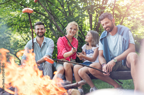 Happy family with male friend roasting sausages over campfire at park © moodboard