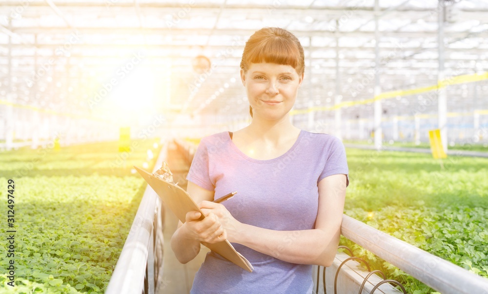Portrait of young female botanist standing with clipboard in plant nursery