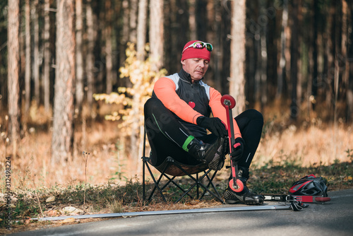 Training an athlete on the roller skaters. Biathlon ride on the roller skis with ski poles, in the helmet. Autumn workout. Roller sport. Adult man riding on skates. Athlete is getting ready to start. photo