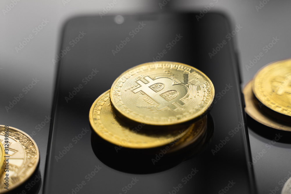 Golden bitcoin coin on a smartphone with a lot of bitcoins coins on a table. Virtual cryptocurrency concept. Mining of bitcoins online bussiness. Bitcoins trading.