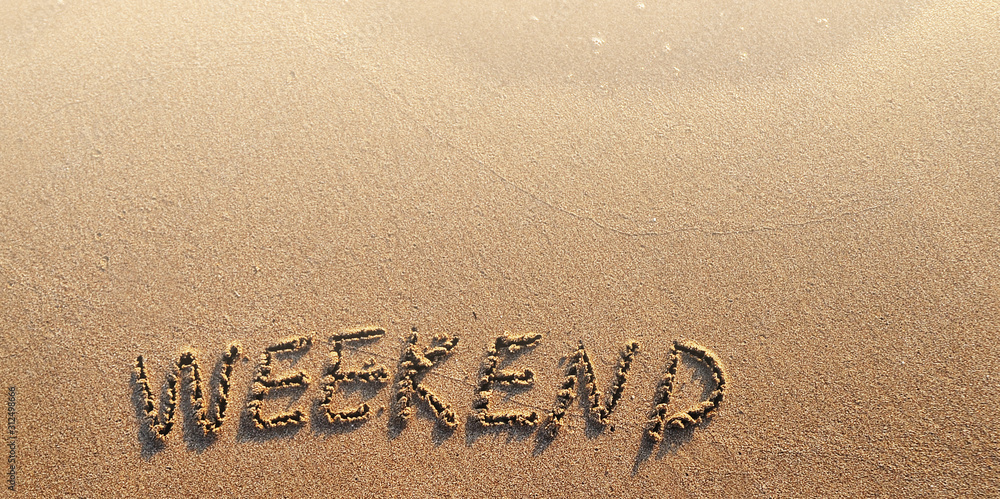 Fototapeta premium The word weekend written on sand. Summertime concept.