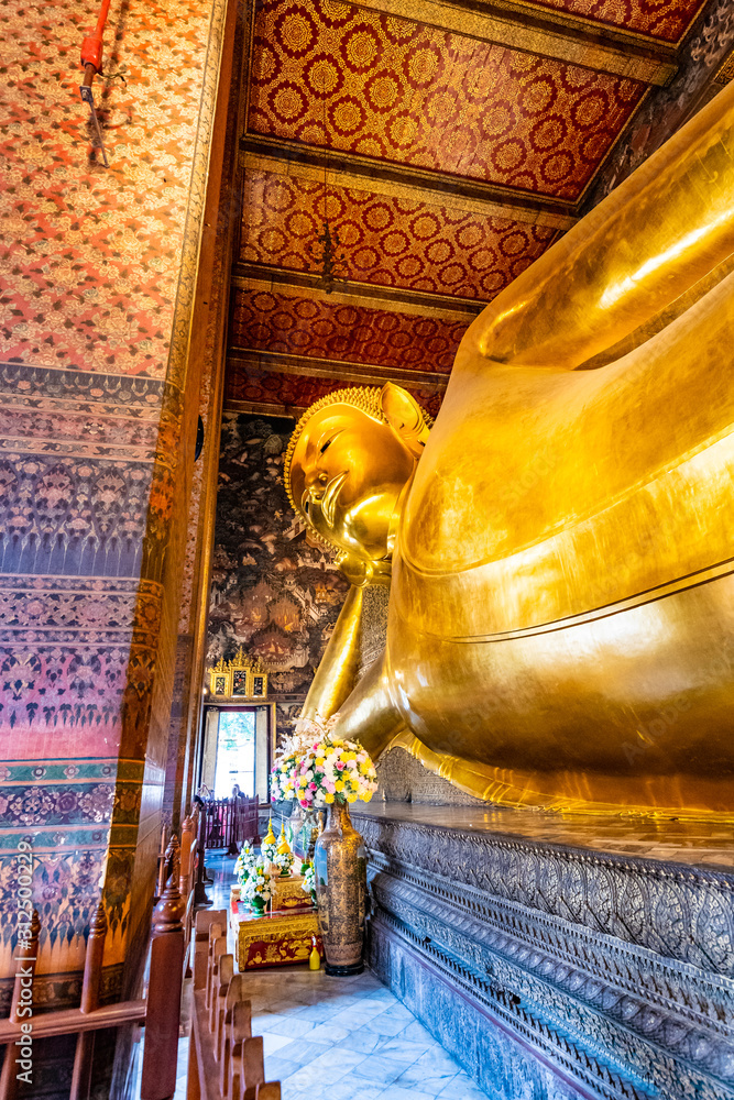Fototapeta premium Beautiful statue of reclining golden Buddha placed in Wat Pho temple, Bangkok. Spiritual place of buddhism religion with beautiful ornaments on the pillar. Detail view of Buddha's head