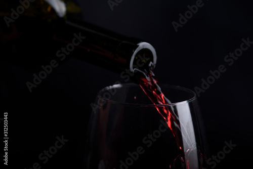 Red wine pouring in wine glass over black background. Closeup of red wine splashing in wineglass in restaurant.