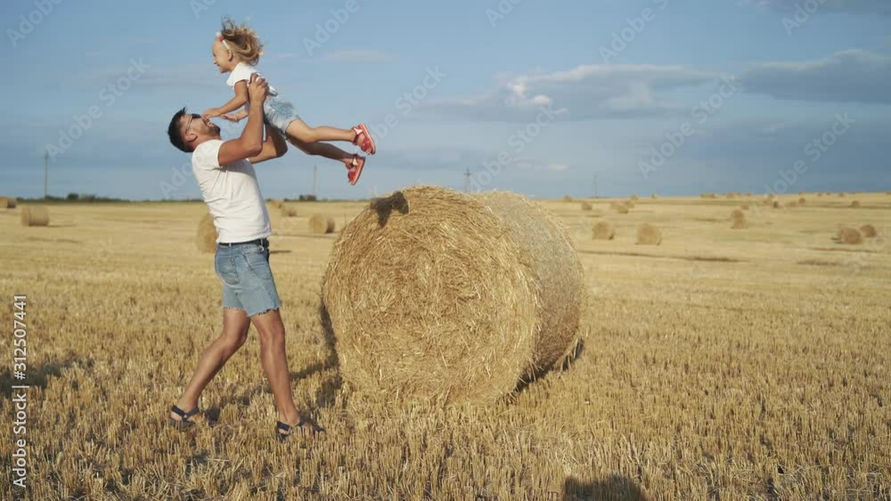 Smiling father throwing up his daughter in field with haycocks Smiling father throwing up his daughter in field with haycocks