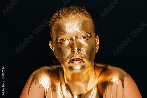 Close up image of young beautiful woman covered with golden paint