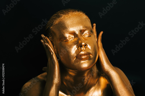 Close up ortait of beautiful woman painted in gold posing as wise monkey symbol