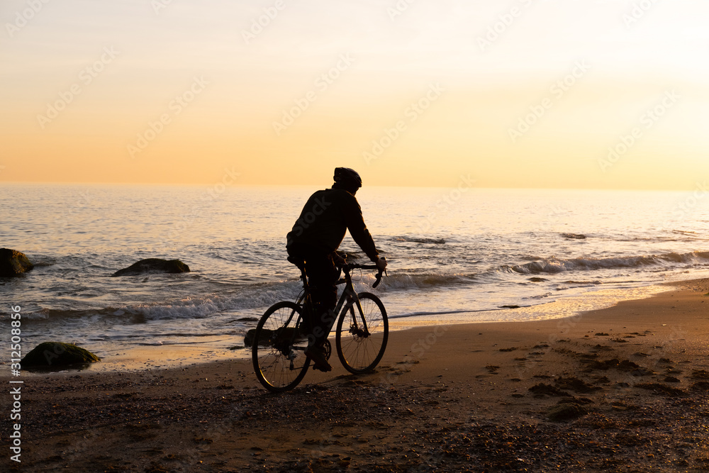 Fototapeta premium silhouette of young male bicycle rider in helmet on the beach during beautiful sunset
