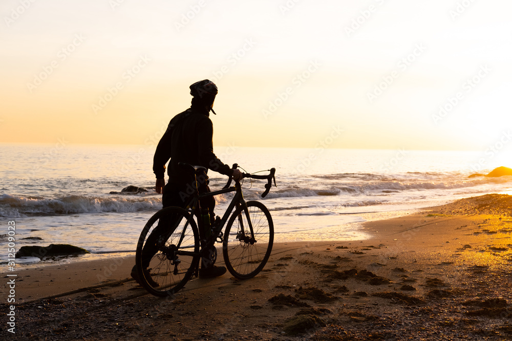 Fototapeta premium silhouette of young male bicycle rider in helmet on the beach during beautiful sunset