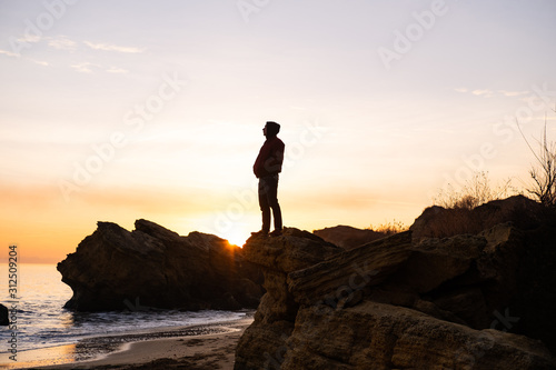 silhouette of male traveler stand near cliff and watch beautiful sunset in the sea