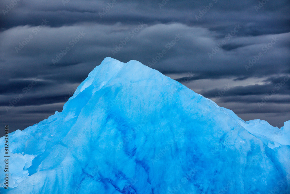 Dark winter mountain with snow, blue glacier ice with sea in the foreground, Svalbard, Norway.
