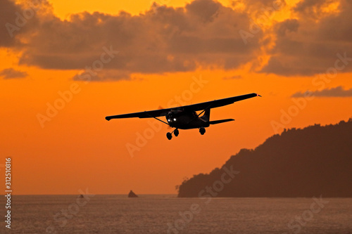 Ait travelling in Costa Rica. Evening sunset in sea coast of Corcovado NP, Costa Rica. Aircraft on the orange sky with dark clouds. Airplane in the wil nature. Forest hill near the ocean water.