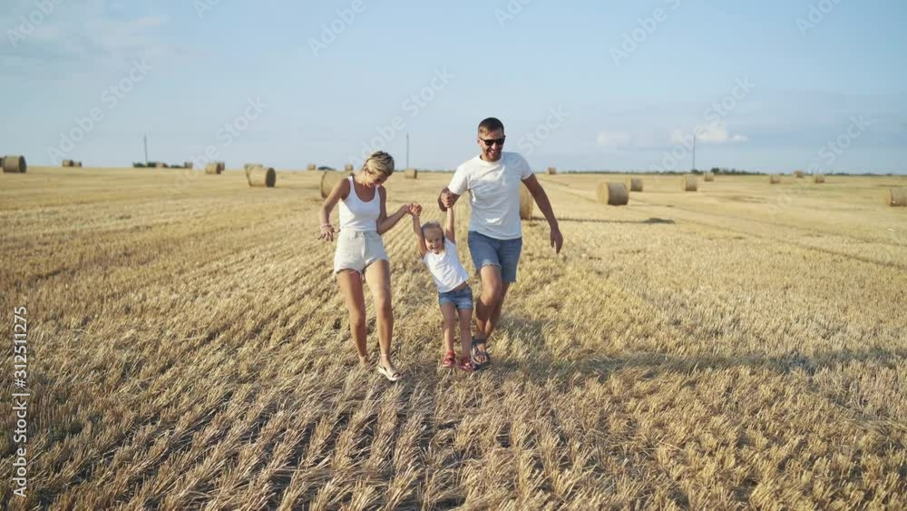 Happy parents hold daughter hands, run and throw hay in huge summer field Happy parents hold daughter hands, run and throw hay in huge summer field