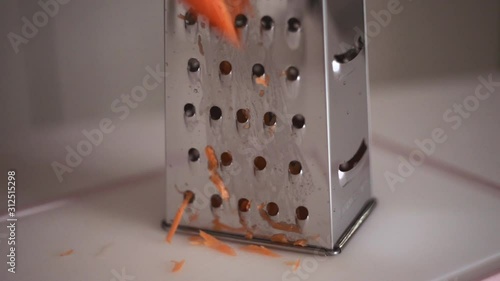 Hands of a young girl rub an orange carrot using a grater. Preparing fresh carrots before cooking on kitchen.