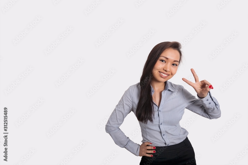 Portrait of happy businesswoman showing victory sign against gray background Portrait of happy businesswoman showing victory sign against gray background