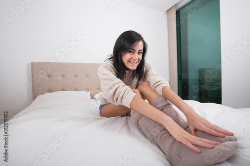Full length portrait of smiling young woman touching feet in bedroom © moodboard