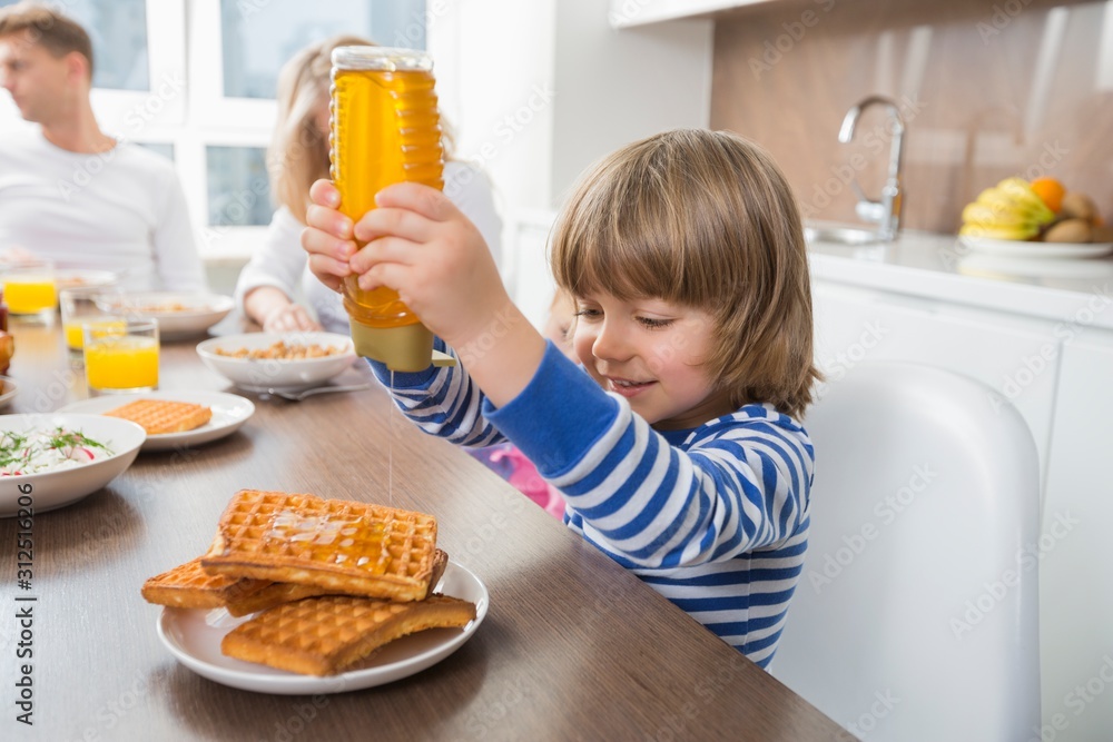 Happy boy pouring honey on waffles while having breakfast with family Happy boy pouring honey on waffles while having breakfast with family