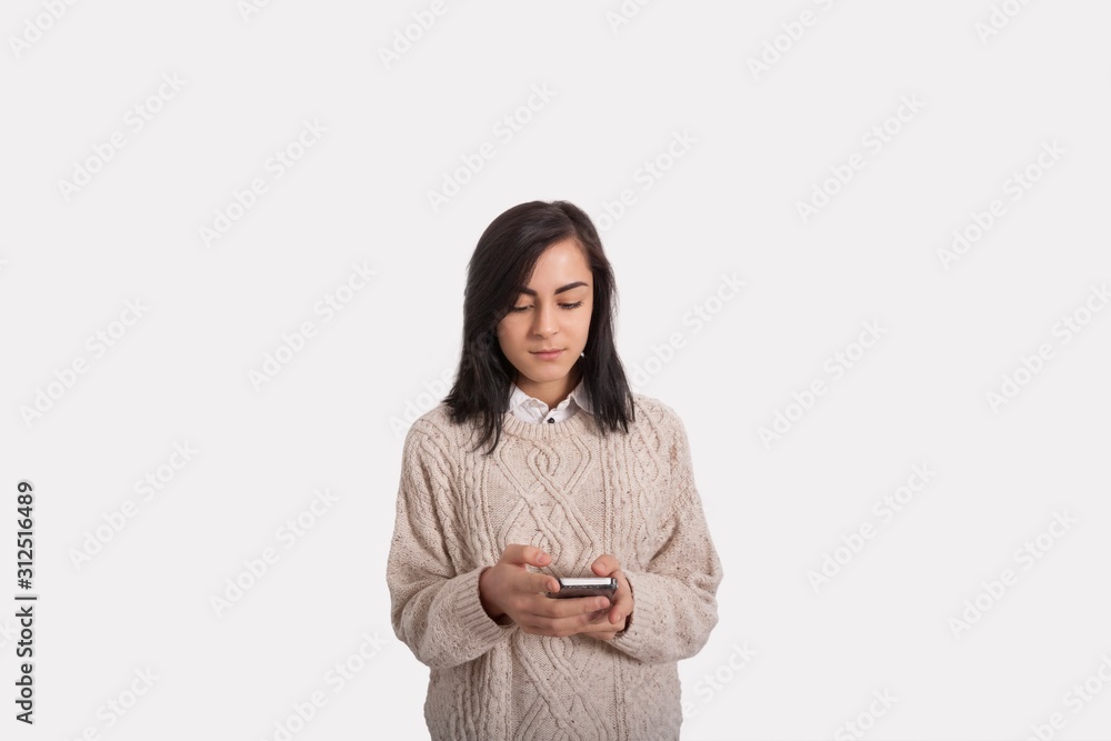 Businesswoman text messaging through smart phone against gray background Businesswoman text messaging through smart phone against gray background