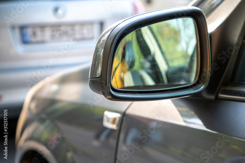 Close up of rearview mirror of a car parked near curb on the side of the street on a parking lot. © bilanol