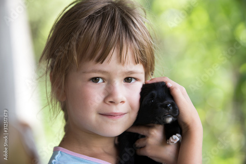 Pretty child girl playing with little puppy outdoors in summer.