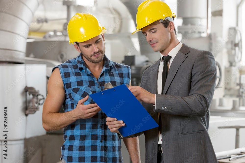 Worker with manager discussing over clipboard in industry Worker with manager discussing over clipboard in industry