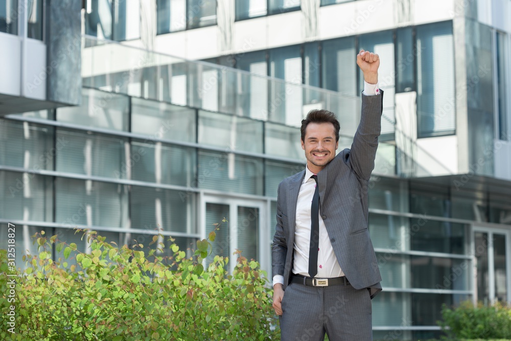 Portrait of cheerful businessman with arm raised standing outside office building Portrait of cheerful businessman with arm raised standing outside office building
