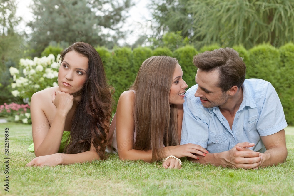Loving young couple ignoring female friend in park Loving young couple ignoring female friend in park
