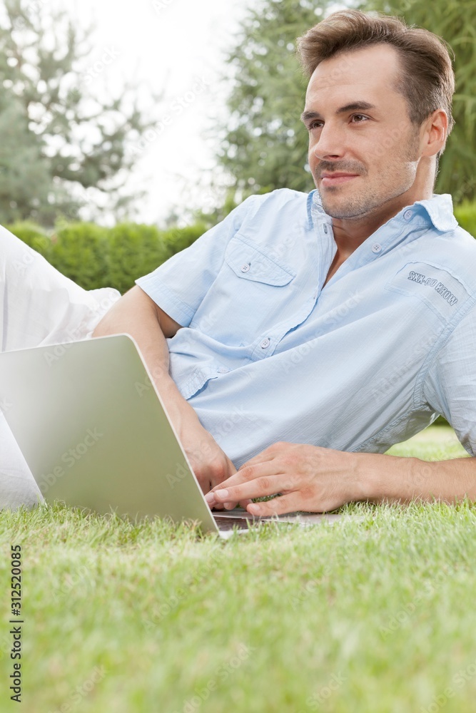 Young man using laptop while looking away in park Young man using laptop while looking away in park